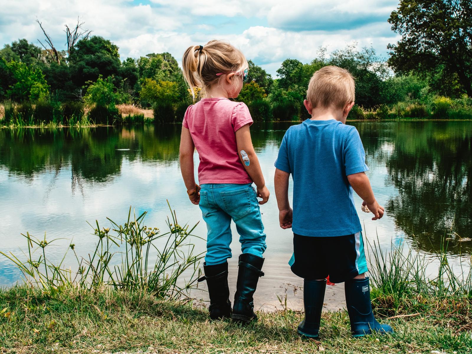 Due bambini in un prato, di fronte ad un lago