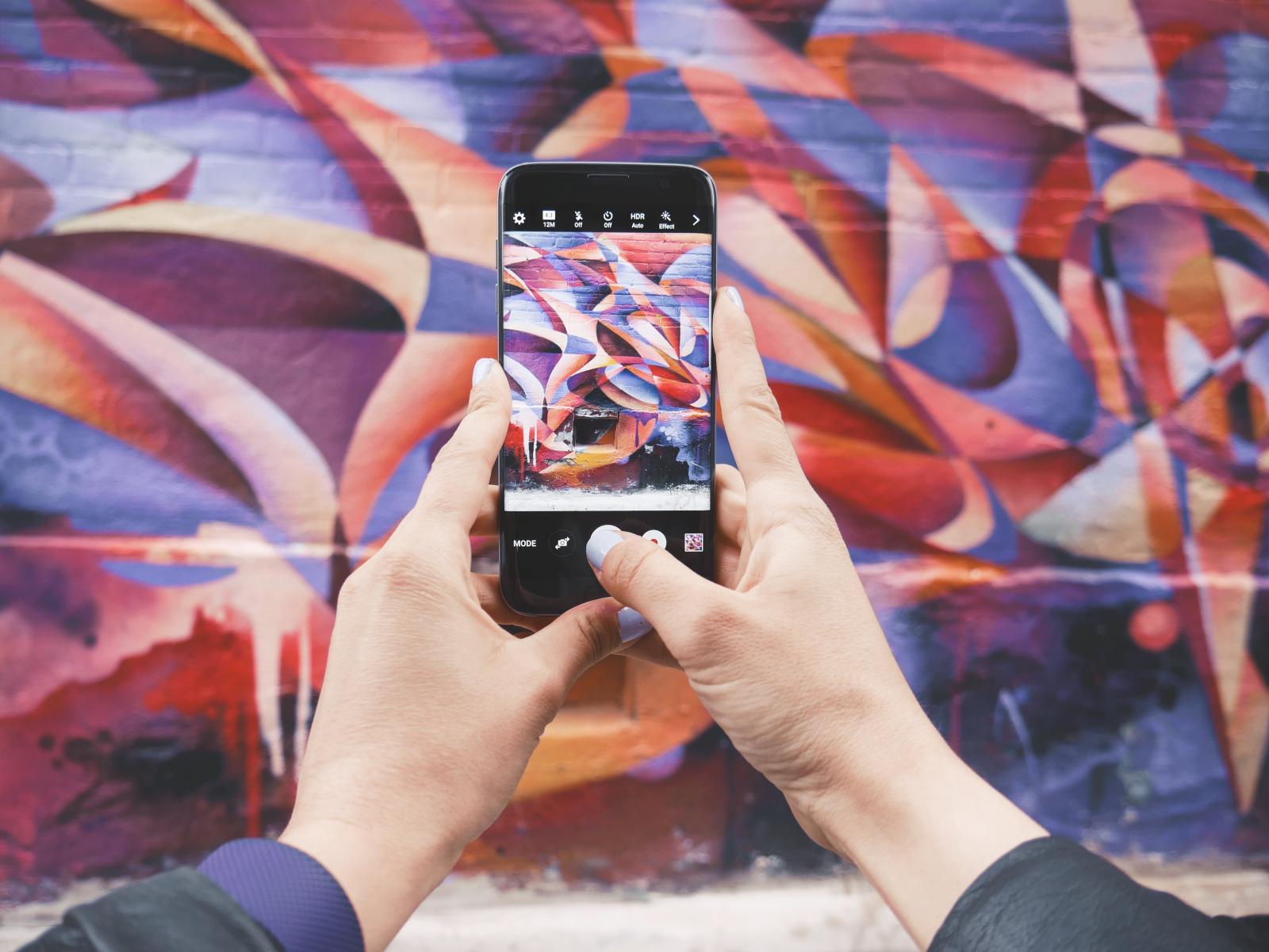 Due mani che afferrano uno smartphone per fare una foto ad un murales colorato