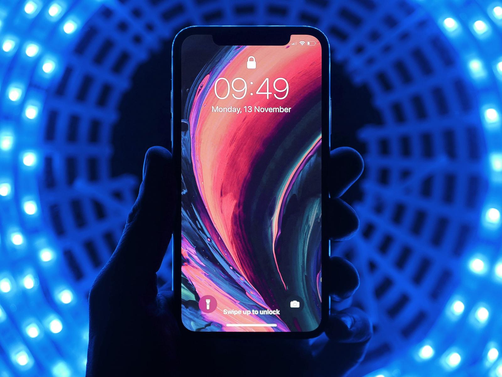 Una mano che afferra uno smartphone, sullo sfondo una luce blu
