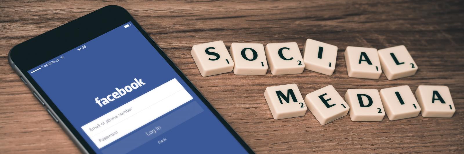 Telefono con App di Facebook aperta, accanto la scritta "social media" creata con le tessere del gioco "Scarabeo"
