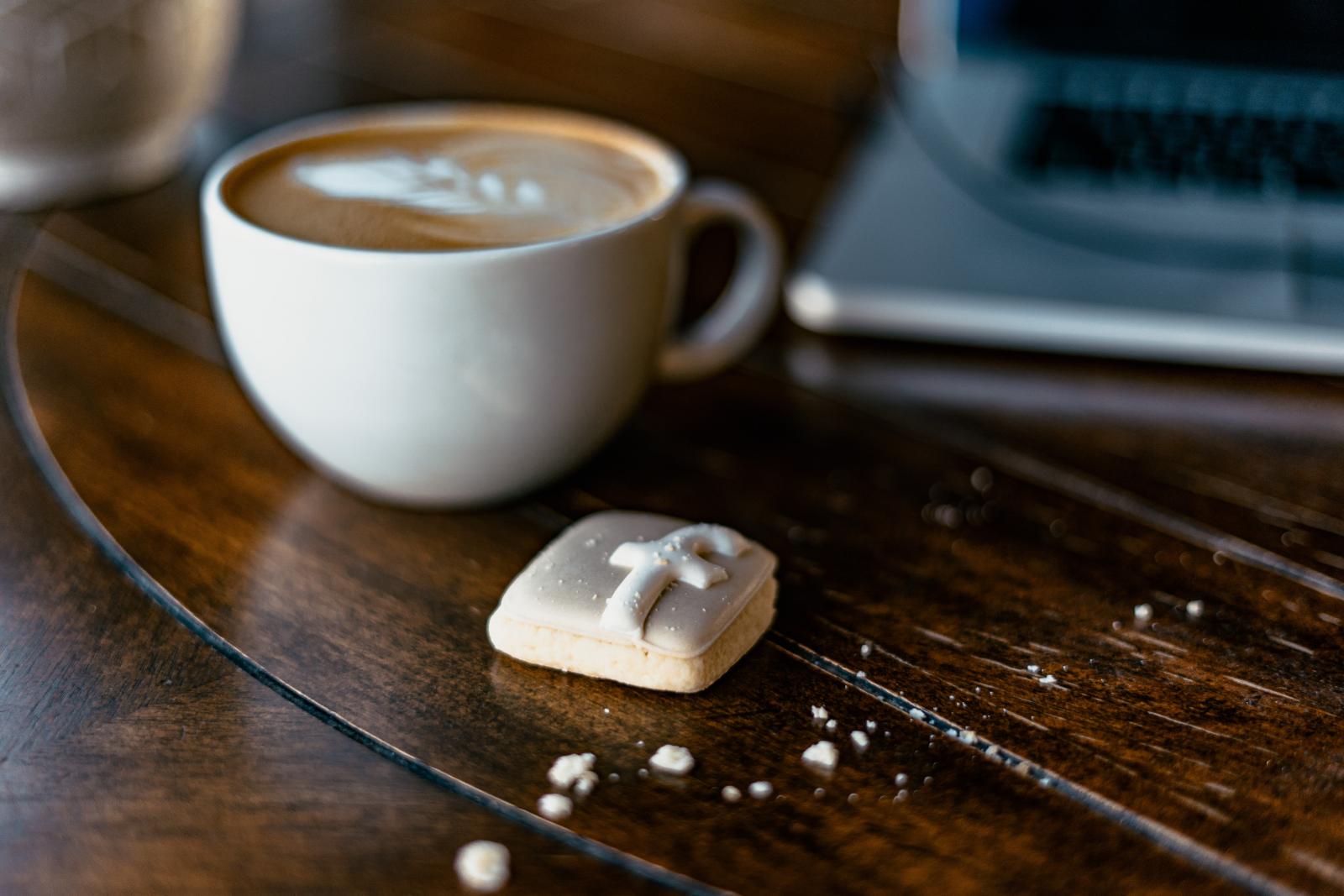 Una tazza di cappuccio, un biscotto con l'icona di facebook e un pc sul tavolo