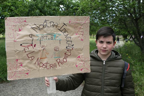 Un ragazzo tiene un manifesto che dice "La nostra identità è la nostra priorità".