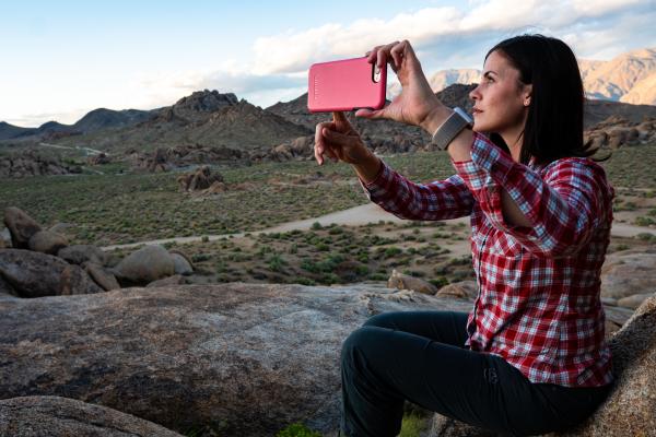 Una ragazza è seduta per terra in montagna e fa una foto al paesaggio con lo smartphone