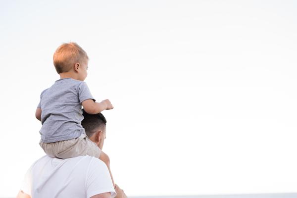 Un ragazzo con una maglie bianca tiene sulle spalle un bambino, entrambi si vedono di spalle