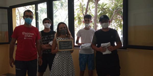 Cinque ragazzi con mascherine protettive, una ragazza tiene in mano una lavagnetta con la scritta "Ottimo lavoro detective"