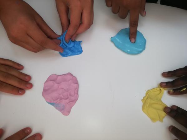 Mani di bambini che toccano slime colorati (rosa, azzurro, blu, giallo).