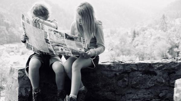 Due ragazzi leggono un giornale seduti su un muretto