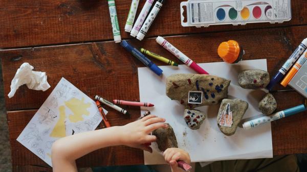 Bambina che gioca e colora con sassi, pastelli, fogli