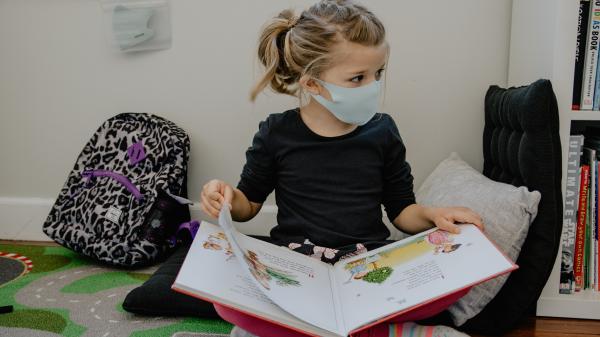 Bambina con una mascherina che legge un libro in classe
